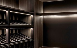 Architectural Joinery Design | Bespoke Timber Wine Cellar Architectural joinery wine cellar featuring dark timber drawers and shelves, a preparation bench, integrated lighting in each section, and abundant custom design wine bottle storage.