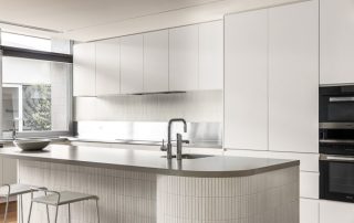 Elevated Kitchen Design: Showcasing Architectural Joinery A minimalist kitchen showcasing a beautiful example of curved joinery in this sculptural kitchen island featuring an integrated sink. Sleek, white kitchen cabinets complete the design.