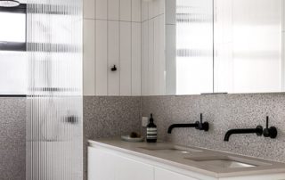 Bespoke Bathroom Vanity | Custom Cabinetry A bathroom vanity with double sinks and natural stone countertop featuring matte black fixtures, two deep drawers and single cabinet, all with a matte white finish.