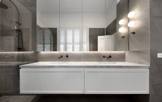 Modern Bathroom Vanity Design with Classic Matte White Finish Close-up of a modern bathroom with brass fixtures, a two sink vanity unit with a white matte finish on the cabinetry unit drawers, and oyster gray marble finish countertop.