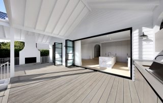 Connecting Indoors & Out: Luxury Living Interior view of a luxury kitchen with oyster gray matte cabinetry and a natural stone island with 'super white' joinery. The open French doors lead to the outdoor entertaining area.