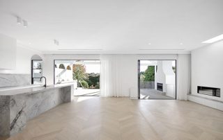 Expansive Entertaining Area with Bespoke Kitchen Island Modern interior with expansive entertaining area, bespoke kitchen island with a super white dolomite benchtop, parquetry floor, and lush views of greenery.