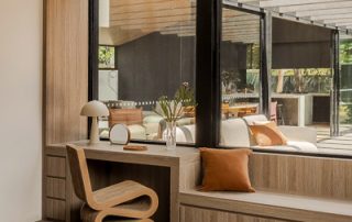 Architectural Joinery | Modern Integrated Window Seat A bespoke window bench-seat and side-desk with integrated window-paneling in a Maison Oak Ravine finish. A sculptural chair sits by the desk with a view to the outdoor entertaining area.
