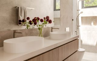 Modern Ensuite Bathroom | Maison Oak Ravine A minimalist ensuite bathroom featuring a floating vanity with dual vessel sinks, a large custom mirror, and a shower area. Natural light flows in through a skylight, enhancing the neutral palette and clean lines.