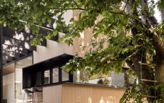 Integrated Indoor-Outdoor Living | Custom Backyard Patio Design An architecturally designed outdoor entertaining area with overhead beams showcasing a bespoke design kitchen pass-through window. The feature is set in natural surrounds with an overhanging tree and rope ladder.