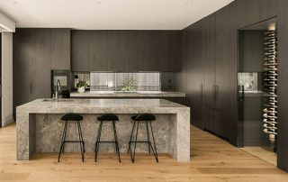 Modern Kitchen | Custom Cabinetry and Fully-Integrated Cellar Luxurious, light-filled kitchen featuring a grey natural stone island with integrated sink and seating for three, and floor-to-ceiling dark finish cabinetry with integrated appliances.