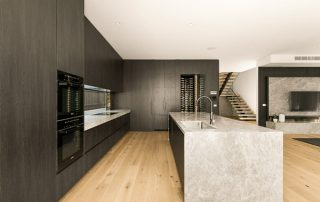 Modern Kitchen Project: Premium Materials and Craftsmanship Modern kitchen with dark cabinets, integrated appliances including a wine refrigerator, and a light natural stone island with a built-in sink.