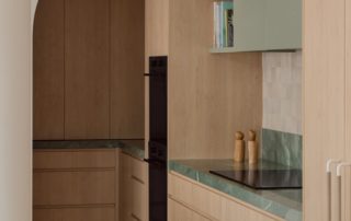 Hampton Residence – Kitchen Full height kitchen cabinetry with integrated appliances, marble splashback and benchtops, and a curved architectural opening.